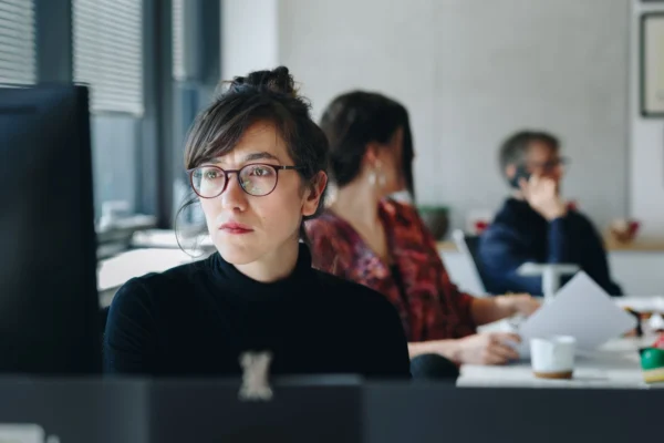 Woman in office with colleagues looking seriously at computer.