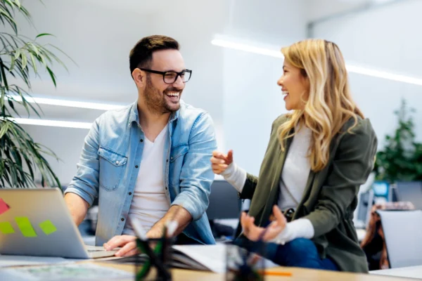 A man and woman laugh in a modern office, representing a comfortable and inclusive working environment.