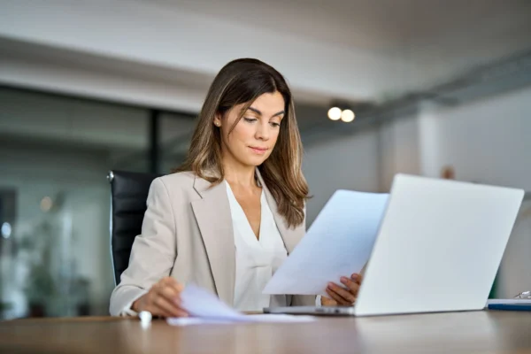 A businesswoman reviewing documents at a desk with a laptop.