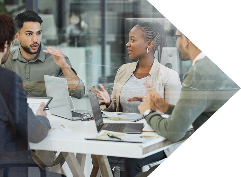 Group of four individuals talking animatedly with open laptops in front of them.
