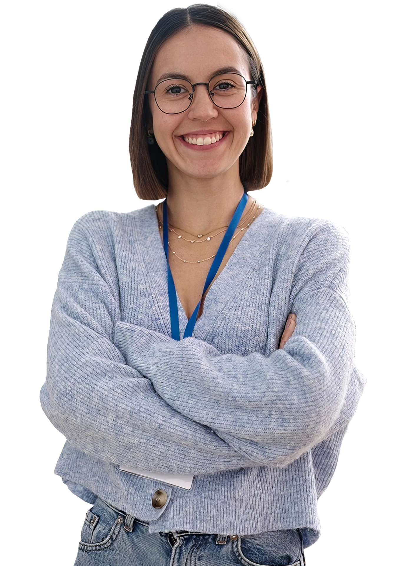 A smiling school teacher, wearing glasses, jeans, and a grey cardigan, with her arms folded.