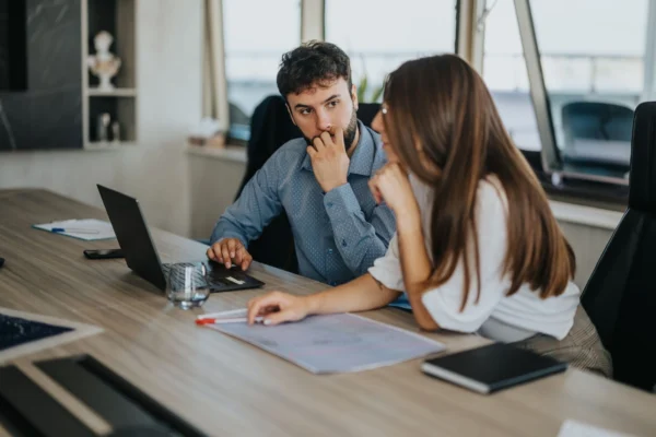 Two employees working together on laptop, one employee is looking concerned.