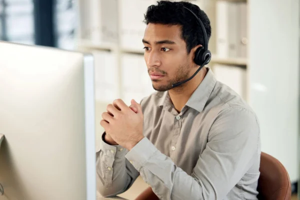 Employee wearing headset sat at laptop looking pensive.