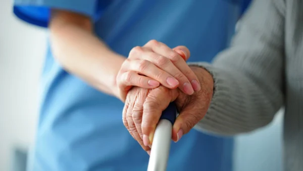 Close up of elderly lady’s hand holding zimmer frame handle, with female nurse’s hand placed caringly on top.