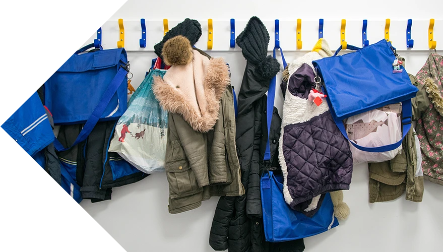 Collection of coats and primary school book bags on a rack of blue and yellow pegs.