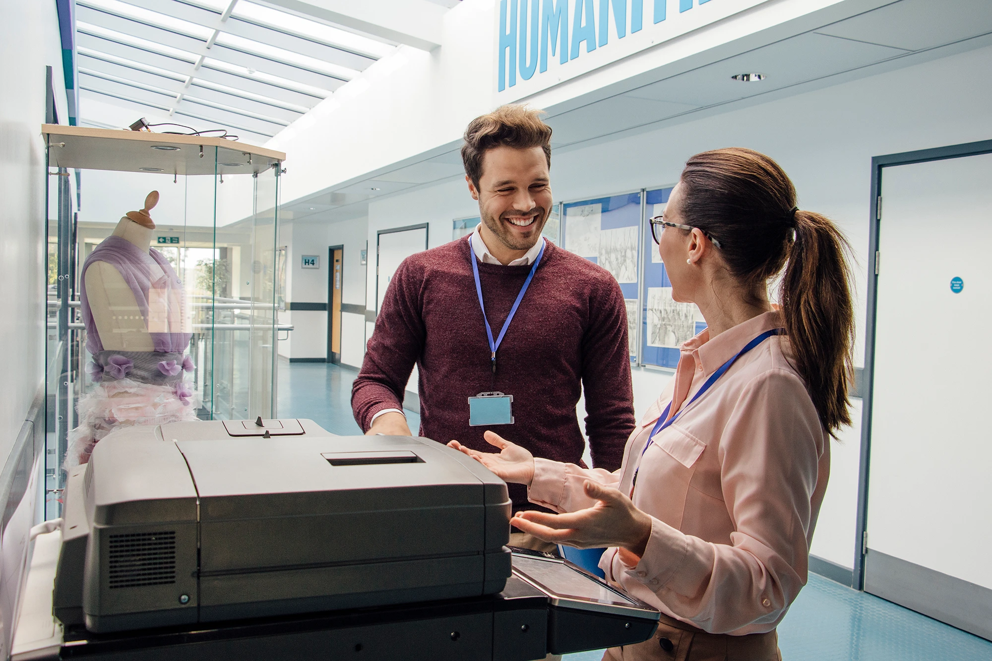 Female school staff member at copying machine chatting to male colleague.