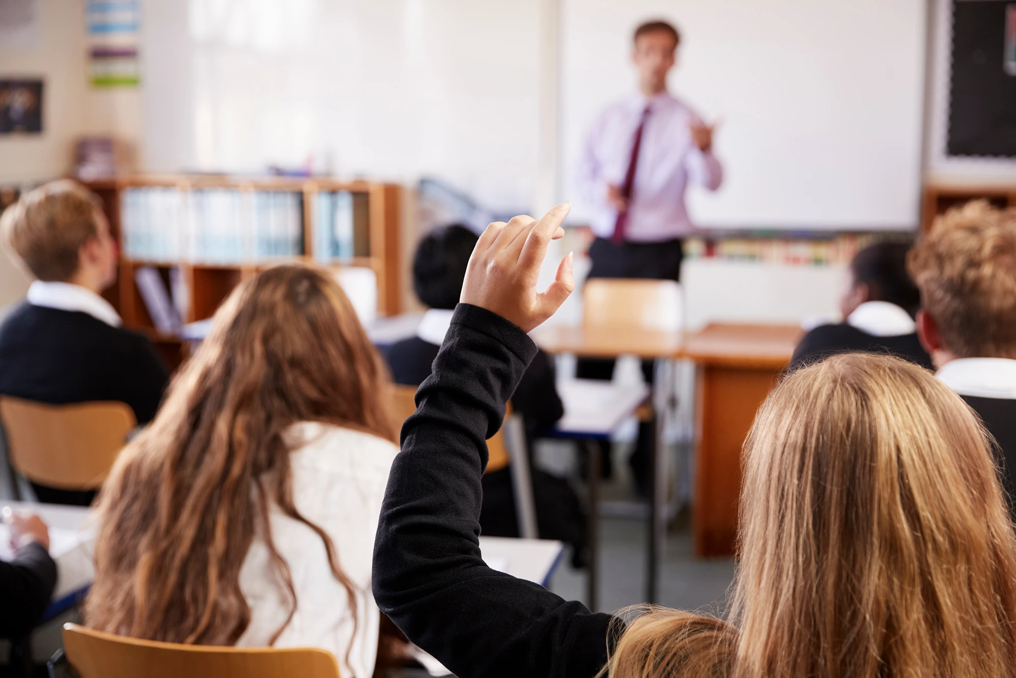 A student raising their hand during a lesson in a classroom.