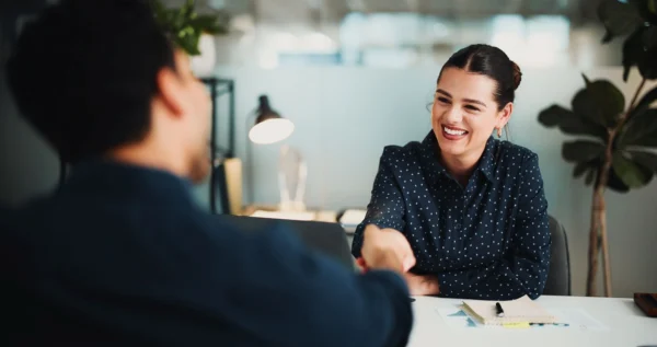 Employee wearing a blue shirt and smiling as she shakes hands with a co-worker.