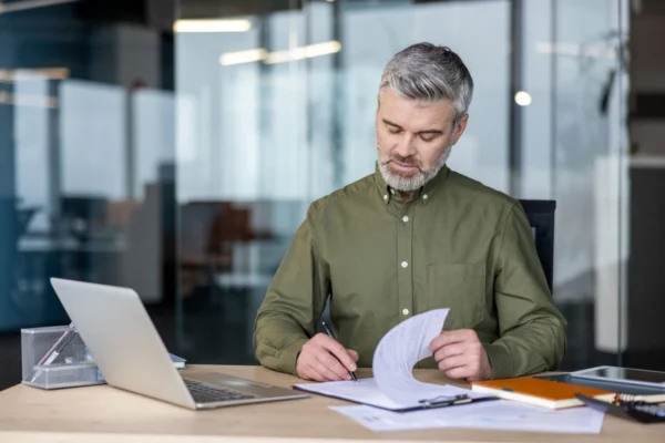 Man with grey hair and green shirt reading form at a desk in a modern office.