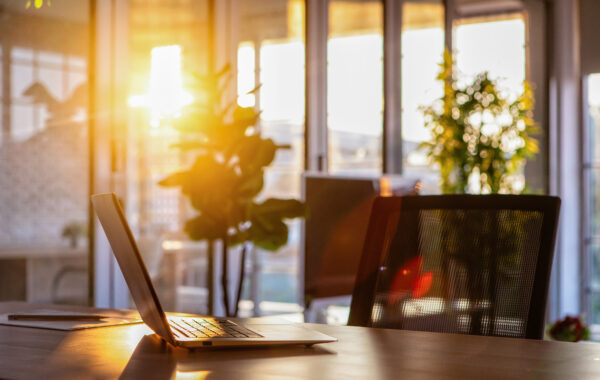 Bright sunlight shining into an office, over a laptop and chair.